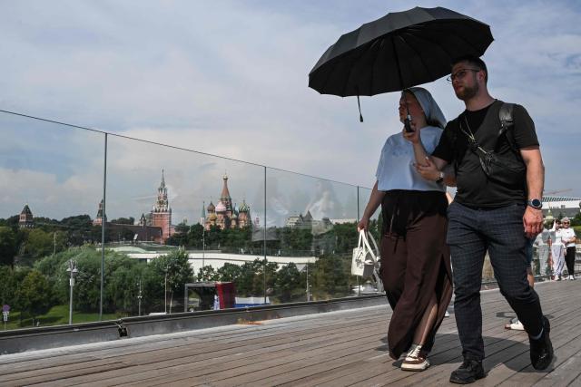 People shelter from the sun under an umbrella as they stroll in Zaryadye park, with the Kremlin in the background, on a hot day in central Moscow on August 7, 2026. (Photo by Igor IVANKO / AFP)