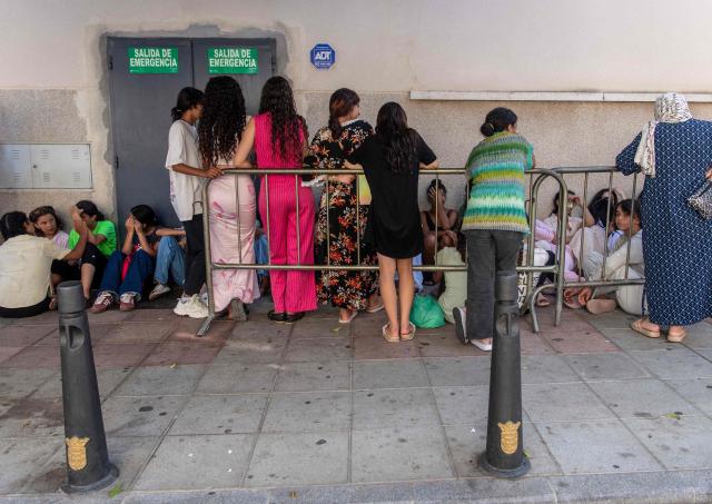Migrant minors wait outside the National Police headquarters to begin identification and registration procedures in the Spanish North African enclave of Ceuta on August 7, 2026, following a mass influx of migrants from Morocco in recent days. Of the 72,000 migrants who reached Ceuta, 70,000 have returned to Morocco, according to official Spanish figures, which have recorded 80 deaths. Morocco's interior ministry has said 11 people died on the Moroccan side of the border, all but one by drowning. Those who remain in Ceuta -- including hundreds of unaccompanied children -- face dire living conditions with little access to food, water, shelter and sanitation. (Photo by Antonio Sempere / AFP)