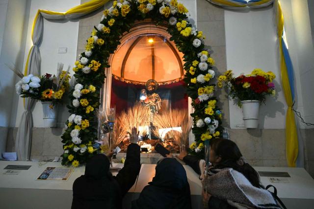 Women touch an image of Saint Cajetan, patron saint of work and bread, as faithful pray at the Saint Cajetan Church in Buenos Aires on August 7, 2026. Every year on the feast of Saint Cajetan, thousands of Catholics visit the shrine to pay homage to the saint and pray for employment and prosperity. (Photo by Luis ROBAYO / AFP)