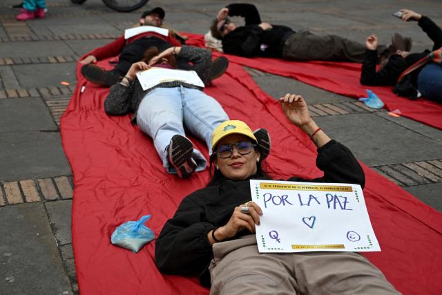 Supporters of outgoing Colombia's President Gustavo Petro take part in a demonstration at Bolivar Square in Bogota on August 7, 2026, lying on colored sheets as part of an installation spelling out the word "Sovereigns", while a participant in the foreground holds a sign reading "For Peace," ahead of the inauguration of Colombian President-elect Abelardo de la Espriella. (Photo by Raul ARBOLEDA / AFP)