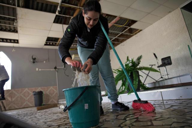 A member of the Evangelical Church Assembleia de Deus Madureira dries the floor as the ceiling remains damaged on August 7, 2026, in Sao Leopoldo, Rio Grande do Sul state, Brazil, after a storm with heavy winds the day before. (Photo by PEDRO H. TESCH / AFP)