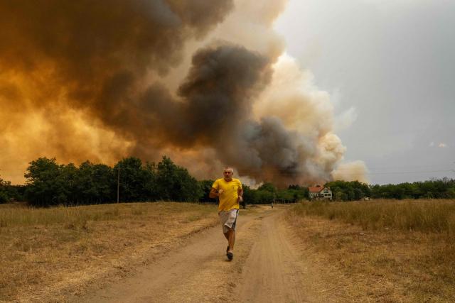A man runs as smoke billows from a wildfire in Deliblatska Pescara (Deliblato Sands), near the village of Sumarak, some 70 kilometres northeast of Belgrade, on August 7, 2026. Firefighters were battling wildfires across the Balkans as days of high temperatures and drought conditions continue to drive blazes in several countries, including Serbia. (Photo by Uros Arsic / AFP)