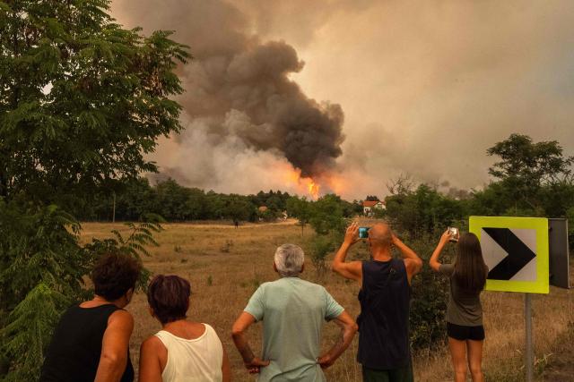 People watch as smoke billows from a wildfire in Deliblatska Pescara (Deliblato Sands), near the village of Sumarak, some 70 kilometres northeast of Belgrade, on August 7, 2026. Firefighters were battling wildfires across the Balkans as days of high temperatures and drought conditions continue to drive blazes in several countries, including Serbia. (Photo by Uros Arsic / AFP)