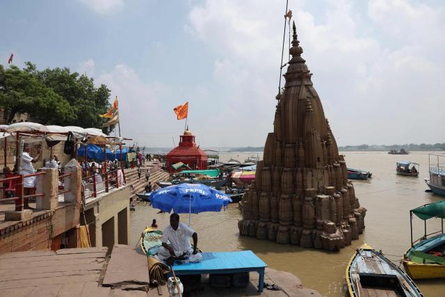 A man sits under an umbrella next to a Hindu temple partially submerged in floodwaters, along the banks of river Ganges in Varanasi on August 8, 2026. (Photo by Niharika KULKARNI / AFP)