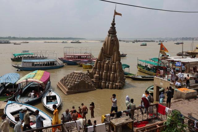 People walk past a Hindu temple partially submerged in floodwaters, along the banks of river Ganges in Varanasi on August 8, 2026. (Photo by Niharika KULKARNI / AFP)