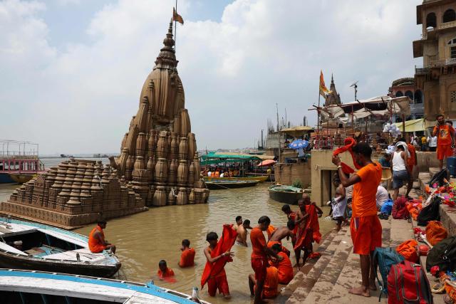 Devotees of the Hindu god Shiva known as 'Kanwariyas' take a holy dip in river Ganges during the 'Kanwar Yatra' pilgrimage, next to a Hindu temple partially submerged in floodwaters in Varanasi on August 8, 2026. (Photo by Niharika KULKARNI / AFP)