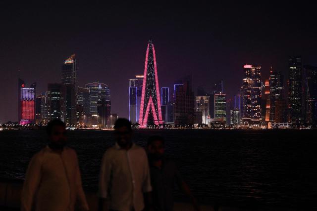 People walk along the Corniche Promenade facing the skyline of illuminated high-rise buildings in Doha on August 8, 2026. (Photo by KARIM JAAFAR / AFP)
