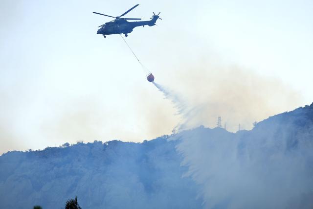 An Albanian army helicopter drops water over a wildfire near the town of Kruje, some 30km northwest of capital Tirana, on August 9, 2026. A 73-year-old man was arrested by the police after setting fire to some weeds in his yard, which then got out of control. Forests catch fire all the more easily because the vegetation and soil have been extremely dry for months, a drought worsened by climate change and the recent exceptional heatwaves. (Photo by Adnan Beci / AFP)