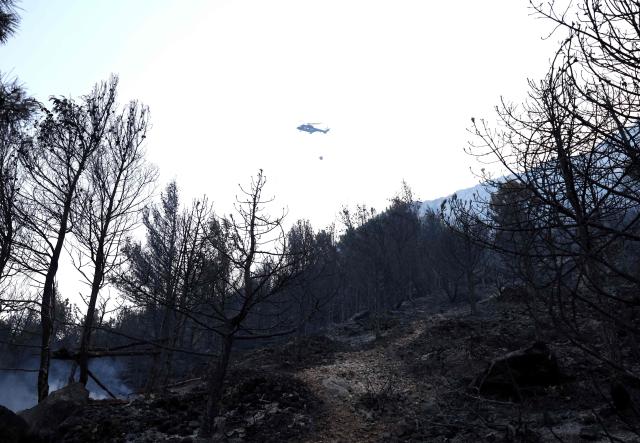 An Albanian army helicopter drops water over a wildfire near the town of Kruje, some 30km northwest of capital Tirana, on August 9, 2026. A 73-year-old man was arrested by the police after setting fire to some weeds in his yard, which then got out of control. Forests catch fire all the more easily because the vegetation and soil have been extremely dry for months, a drought worsened by climate change and the recent exceptional heatwaves. (Photo by Adnan Beci / AFP)