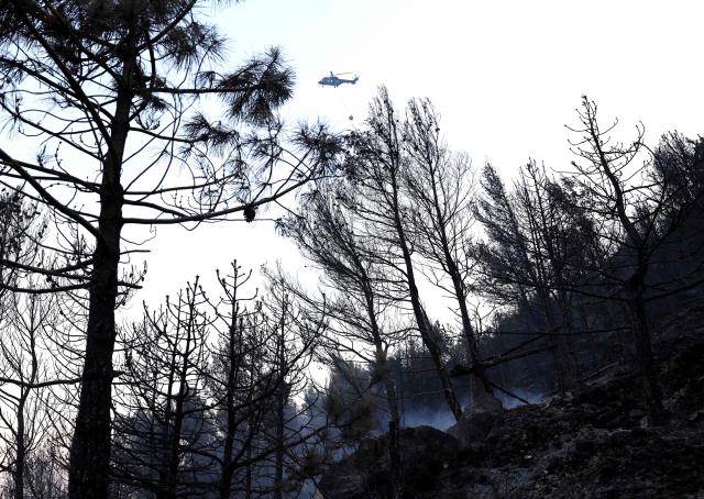 An Albanian army helicopter drops water over a wildfire near the town of Kruje, some 30km northwest of capital Tirana, on August 9, 2026. A 73-year-old man was arrested by the police after setting fire to some weeds in his yard, which then got out of control. Forests catch fire all the more easily because the vegetation and soil have been extremely dry for months, a drought worsened by climate change and the recent exceptional heatwaves. (Photo by Adnan Beci / AFP)