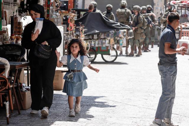 A Palestinian youth watches as armed Israeli soldiers carry out a foot patrol through the market, in the Old City of Nablus, in the northern Israeli-occupied West Bank on August 9, 2026. The occupied West Bank has been gripped by almost daily violence involving Israeli troops and settlers since the start of the Gaza war in October 2023. Israel has occupied the West Bank since 1967, but in recent years the number of Israeli settlements in the Palestinian territory -- which are illegal under international law -- has soared. (Photo by Jaafar ASHTIYEH / AFP)