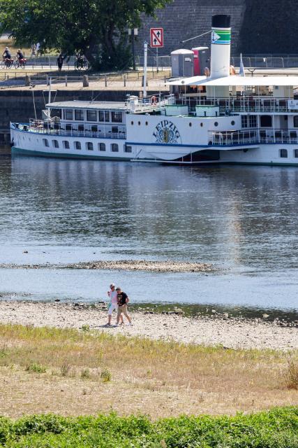 People walk on the long riverbed of the river Elbe, as a passengers ship is docked on the dock in Dresden, eastern Germany, on August 9, 2026, with hot and dry weather conditions keeping very low the water level of the river. (Photo by Jens SCHLÜTER / AFP)