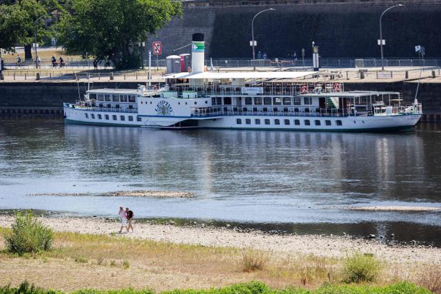People walk on the long riverbed of the river Elbe, as a passengers ship is docked on the dock in Dresden, eastern Germany, on August 9, 2026, with hot and dry weather conditions keeping very low the water level of the river. (Photo by Jens SCHLÜTER / AFP)