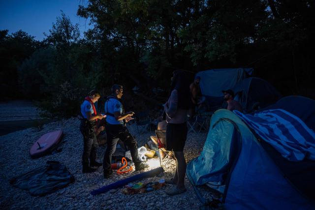 French gendarmes check on tourists to prevent wild camping and forest fire risks around Lake Sainte-Croix, southeastern France on August 8, 2026. At nightfall, two gendarmes scan the shores of Lake Sainte-Croix—located at the gateway to the Verdon Gorge—with binoculars, looking for potential campers. Their mission: to prevent any illegal camping that could spark a fire in the surrounding woodlands. (Photo by Miguel MEDINA / AFP)