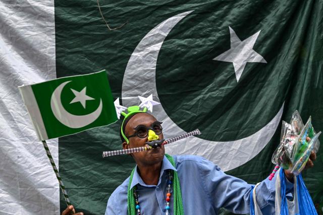 A vendor selling toys stands near the Pakistani national flag at a marketplace in Lahore on August 9, 2026 ahead of the country's Independence Day celebration. (Photo by Arif ALI / AFP)