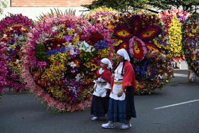 Women walk past traditional flower arrangements known as "silletas" displayed ahead of the Silleteros Parade during the Flower Festival in Medellin, Antioquia department, Colombia, on August 9, 2026. (Photo by Jaime SALDARRIAGA / AFP)