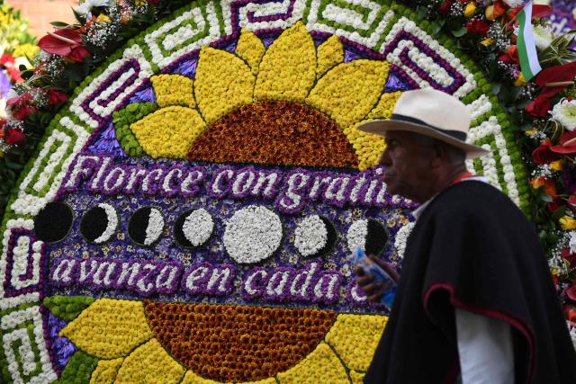 A farmer walks past a traditional flower arrangement known as a "silleta" during the Silleteros Parade held as part of the Flower Festival in Medellin, Antioquia department, Colombia, on August 9, 2026. (Photo by Jaime SALDARRIAGA / AFP)