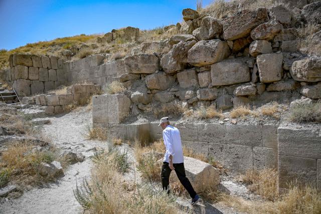 Mehmet Kusman, aged 86, who speaks Urartian language, walks past remains of the fortress of Cavustepe near Van, in eastern Turkey, on July 22, 2026. Mehmet Kusman, 86, has dedicated his life to the Cavustepe Fortress in eastern Turkey and to studying the Urartian language, which borrows its cuneiform alphabet from Assyrian to honor the gods and rulers of the lost kingdom. (Photo by Ozan KOSE / AFP)