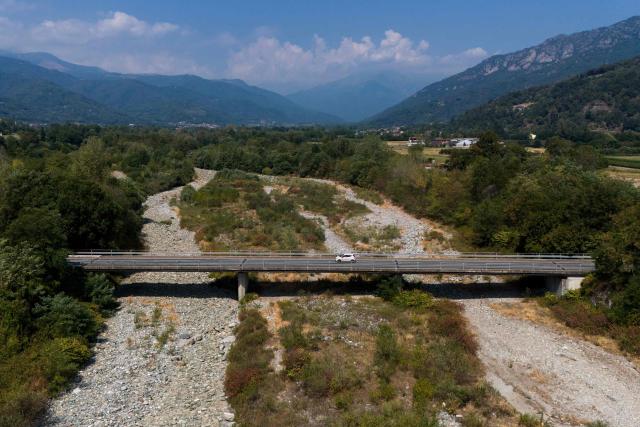(FILES) This aerial view shows a car crossing the bridge over the Po River in Martiniana Po, on July 30, 2026. The Po Valley in northern Italy is facing a severe water and drought crisis driven by intense summer heatwaves and sparse rainfall. Water levels and river flow have plummeted rapidly, exposing sandbanks and triggering urgent concerns for regional agriculture and ecosystems. Climate change has intensified a drought across Europe this summer, with extreme heat driving the exceptionally dry conditions, according to experts. (Photo by Marco Bertorello / AFP)