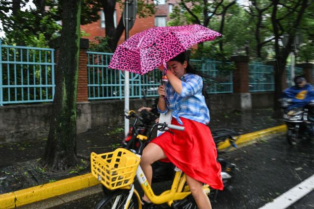 A woman uses an umbrella to shelter from the rain while riding a bicycle along a road a day after Typhoon Dolphin made landfall in Shanghai on August 10, 2026. (Photo by Hector RETAMAL / AFP)