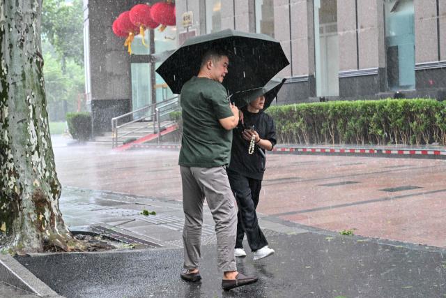 People use umbrellas to shelter from the rain as they walk on a street a day after Typhoon Dolphin made landfall in Shanghai on August 10, 2026. (Photo by Hector RETAMAL / AFP)