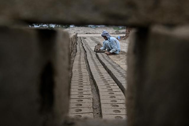 A man works at a brick kiln in Sheikhupura, in Pakistan’s Punjab province on July 20, 2026. Below dark plumes billowing from smokestacks, brick workers on a kiln in Pakistan's Sheikhupura district crush coal through small holes into the fiery chambers below. Despite the scorching sun and dust filling the hot air, they stay on the heated surface for hours at a time, trapped in a cycle of debt, extreme heat, and deteriorating health, with rising global temperatures amplifying the risks. (Photo by Arif ALI / AFP)