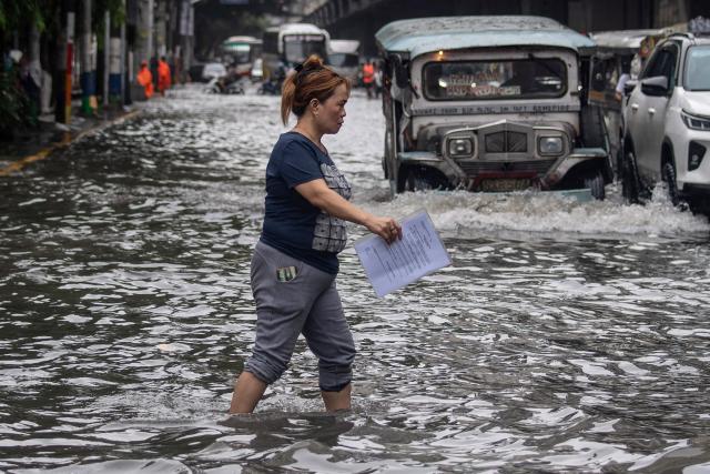 A pedestrian crosses a flooded street after heavy rain in Manila on August 10, 2026. (Photo by Ted ALJIBE / AFP)