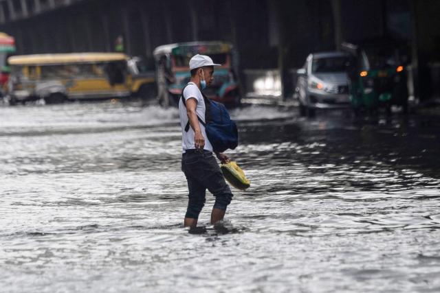 A pedestrian crosses a flooded street after heavy rain in Manila on August 10, 2026. (Photo by Ted ALJIBE / AFP)