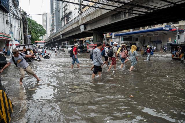 Pedestrians cross a flooded street after heavy rain in Manila on August 10, 2026. (Photo by Ted ALJIBE / AFP)