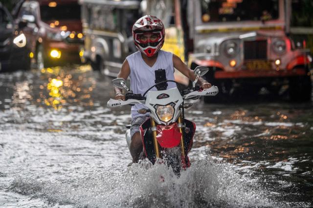 A motorist commutes along a flooded street after heavy rain in Manila on August 10, 2026. (Photo by Ted ALJIBE / AFP)