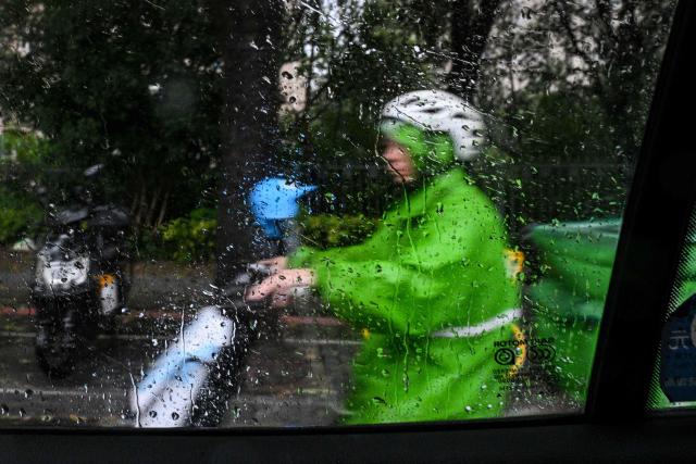 A man riding a scooter is seen through rain on the window of a taxi a day after Typhoon Dolphin made landfall in Shanghai on August 10, 2026. (Photo by Hector RETAMAL / AFP)