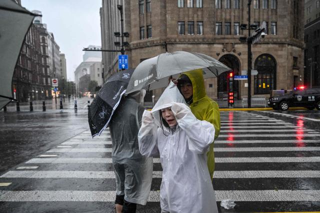 People visit the Bund amid heavy rain a day after Typhoon Dolphin made landfall in Shanghai on August 10, 2026. (Photo by Hector RETAMAL / AFP)