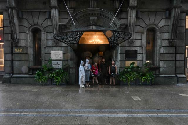 People take shelter from the rain on the Bund a day after Typhoon Dolphin made landfall in Shanghai on August 10, 2026. (Photo by Hector RETAMAL / AFP)