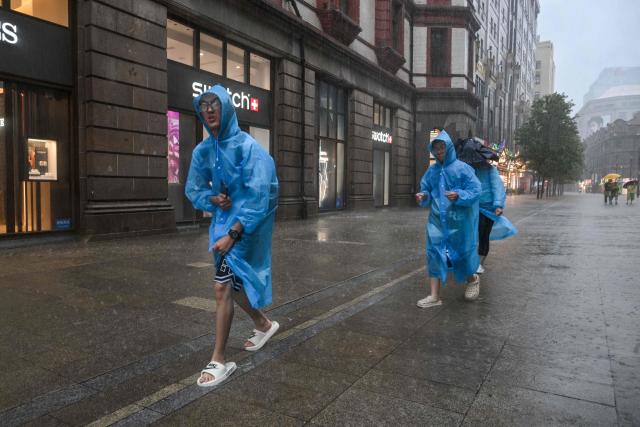 People visit the Bund amid heavy rain a day after Typhoon Dolphin made landfall in Shanghai on August 10, 2026. (Photo by Hector RETAMAL / AFP)