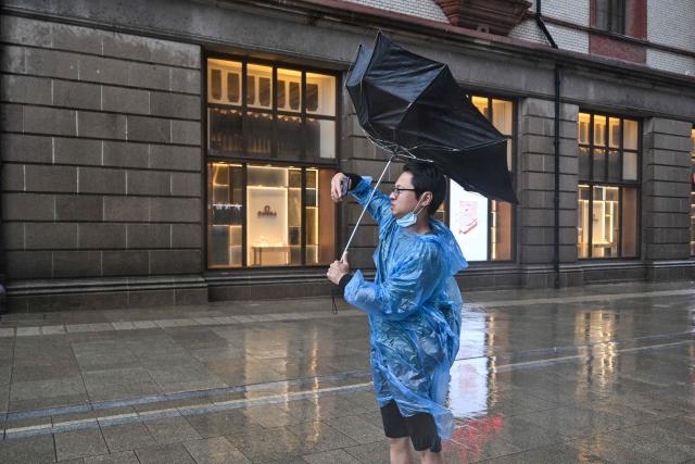 A man uses an umbrella to shelter from the rain on the Bund a day after Typhoon Dolphin made landfall in Shanghai on August 10, 2026. (Photo by Hector RETAMAL / AFP)