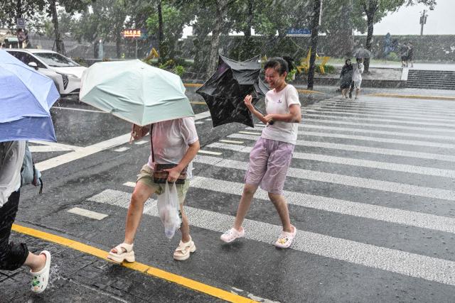 People use umbrellas to shelter from the rain as they walk on The Bund a day after Typhoon Dolphin made landfall in Shanghai on August 10, 2026. (Photo by Hector RETAMAL / AFP)