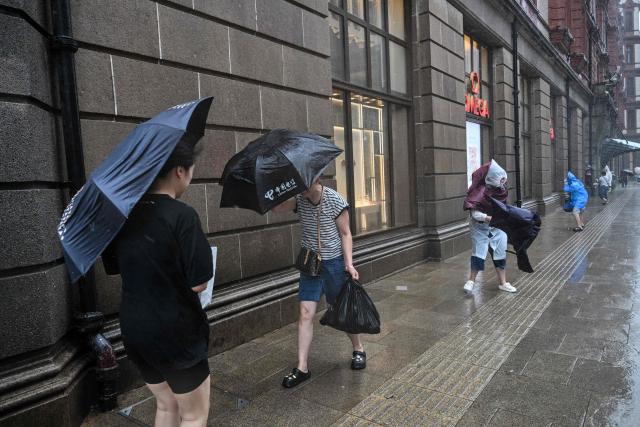People use umbrellas to shelter from the rain on the Bund a day after Typhoon Dolphin made landfall in Shanghai on August 10, 2026. (Photo by Hector RETAMAL / AFP)