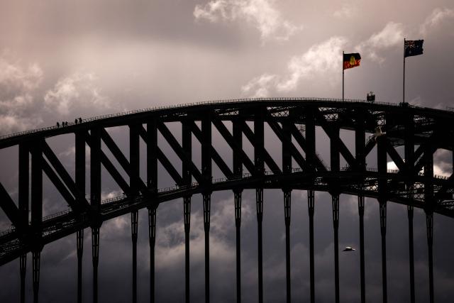 People stand on the arch of the Sydney Harbour Bridge as storm clouds approach on a windy winter's day in Sydney on August 10, 2026. (Photo by DAVID GRAY / AFP)