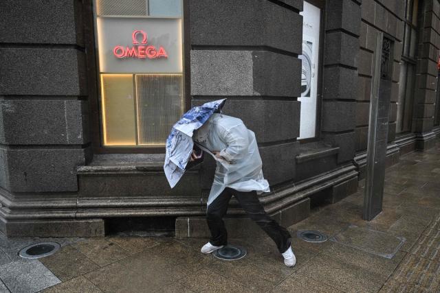 A person uses an umbrella to shelter from the rain and wind on the Bund a day after Typhoon Dolphin made landfall in Shanghai on August 10, 2026. (Photo by Hector RETAMAL / AFP)
