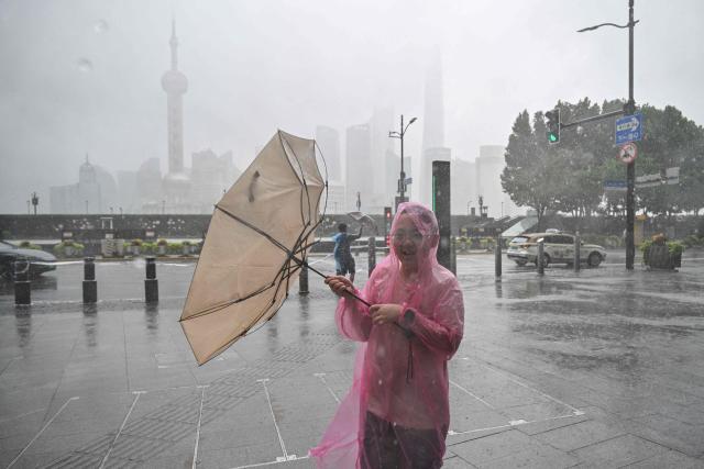 People use umbrellas to shelter from the rain as they walk on the Bund a day after Typhoon Dolphin made landfall in Shanghai on August 10, 2026. (Photo by Hector RETAMAL / AFP)