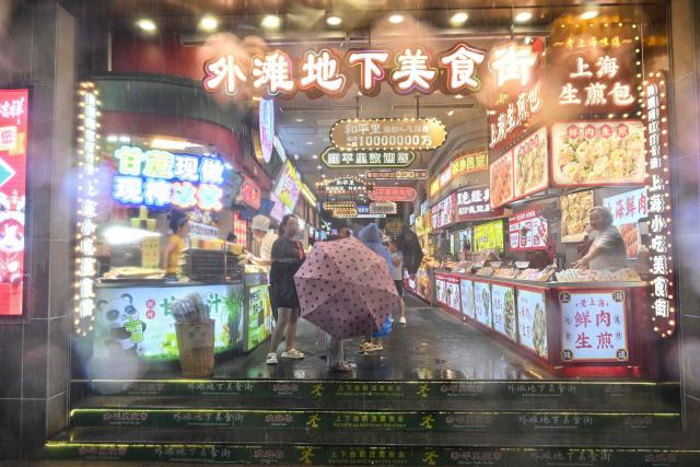 People take shelter from the rain and wind in a restaurant area on the Bund a day after Typhoon Dolphin made landfall in Shanghai on August 10, 2026. (Photo by Hector RETAMAL / AFP)