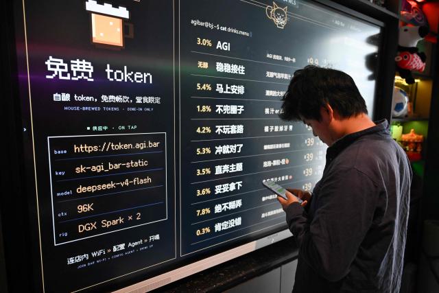 A customer uses his phone in front of a board with the menu at AGI Bar in Beijing's in Zhongguancun district on August 9, 2026. Artificial intelligence users are shopping around as US giants face fierce competition from Chinese rivals -- and in Beijing's tech district, drinkers at an AI-themed bar can even plug in to DeepSeek for free. (Photo by Pedro PARDO / AFP) / To go with AFP story  China-US-technology-AI-business, FOCUS by Luna Lin and Thomas Urbain