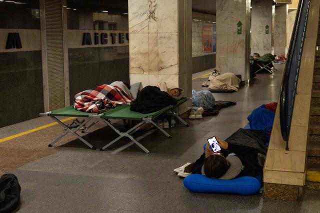 A person checks a smartphone and others sleep as they take shelter overnight in a Kyiv metro station, following warnings of a possible Russian air attack, on early August 10, 2026, amid the Russian invasion of Ukraine. By sunrise, no large-scale attack had taken place on the capital as warnings continued for the coming days. (Photo by Serhii Okunev / AFP)