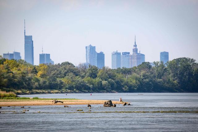 People sit on the bank of the Vistula river just outside the capital Warsaw on August 10, 2026. The Vistula, Poland's longest river, fell on Monday to match its record low in Warsaw, the national meteorological institute IMGW reported, with Europe sweltering through multiple heatwaves. (Photo by Mladen ANTONOV / AFP)