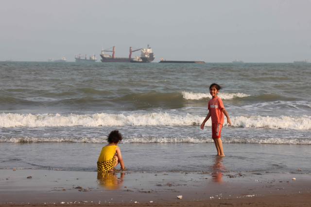 Iranian children enjoy a dip in the sea as vessels are seen in the Strait of Hormuz off Bandar Abbas, in southern Iran on August 10, 2026. The US President signalled on August 9 that he was prepared to let economic pressure mount against Iran, apparently backing away from more military strikes after Tehran issued a list of demands for opening the Strait of Hormuz. His remarks came after Iran issued over the weekend a list of conditions to reopen the Strait of Hormuz, which has remained largely closed since the start of the Middle East war in late February. (Photo by Atta KENARE / AFP) / 