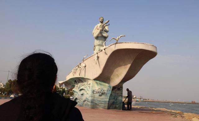 A man stands in the shade of a sculpture erected along the seafront in the port city of Bandar Abbas, in southern Iran on August 10, 2026. The US President signalled on August 9 that he was prepared to let economic pressure mount against Iran, apparently backing away from more military strikes after Tehran issued a list of demands for opening the Strait of Hormuz. His remarks came after Iran issued over the weekend a list of conditions to reopen the Strait of Hormuz, which has remained largely closed since the start of the Middle East war in late February. (Photo by Atta KENARE / AFP) / 