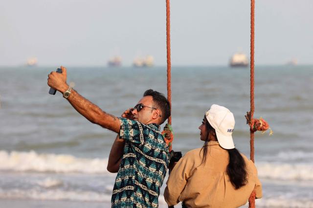 Iranians take a selfie along the shoreline as vessels are seen in the Strait of Hormuz off the port city of Bandar Abbas, in southern Iran on August 10, 2026. The US President signalled on August 9 that he was prepared to let economic pressure mount against Iran, apparently backing away from more military strikes after Tehran issued a list of demands for opening the Strait of Hormuz. His remarks came after Iran issued over the weekend a list of conditions to reopen the Strait of Hormuz, which has remained largely closed since the start of the Middle East war in late February. (Photo by Atta KENARE / AFP) / 