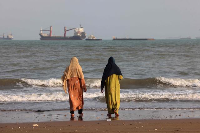 Iranians enjoy the seashore as vessels are seen in the Strait of Hormuz off Bandar Abbas, in southern Iran on August 10, 2026. The US President signalled on August 9 that he was prepared to let economic pressure mount against Iran, apparently backing away from more military strikes after Tehran issued a list of demands for opening the Strait of Hormuz. His remarks came after Iran issued over the weekend a list of conditions to reopen the Strait of Hormuz, which has remained largely closed since the start of the Middle East war in late February. (Photo by Atta KENARE / AFP) / 