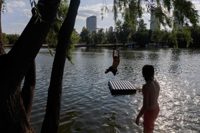 Teenagers play on a rope swing as they swim in Telbin lake on a hot day in Kyiv on August 10, 2026, amid the Russian invasion of Ukraine. (Photo by Tetiana DZHAFAROVA / AFP)