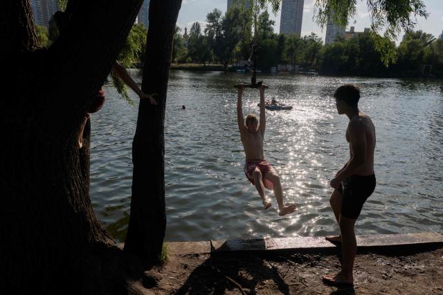 Teenagers play on a rope swing as they swim in Telbin lake on a hot day in Kyiv on August 10, 2026, amid the Russian invasion of Ukraine. (Photo by Tetiana DZHAFAROVA / AFP)